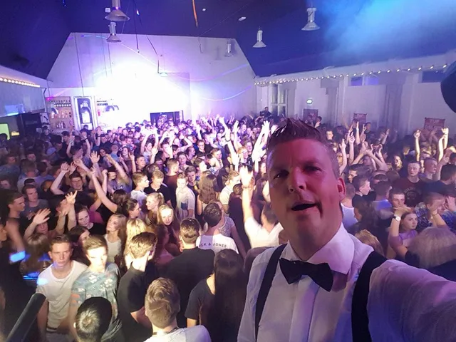 Sjon in overhemd en strik met een volle zaal achter zich